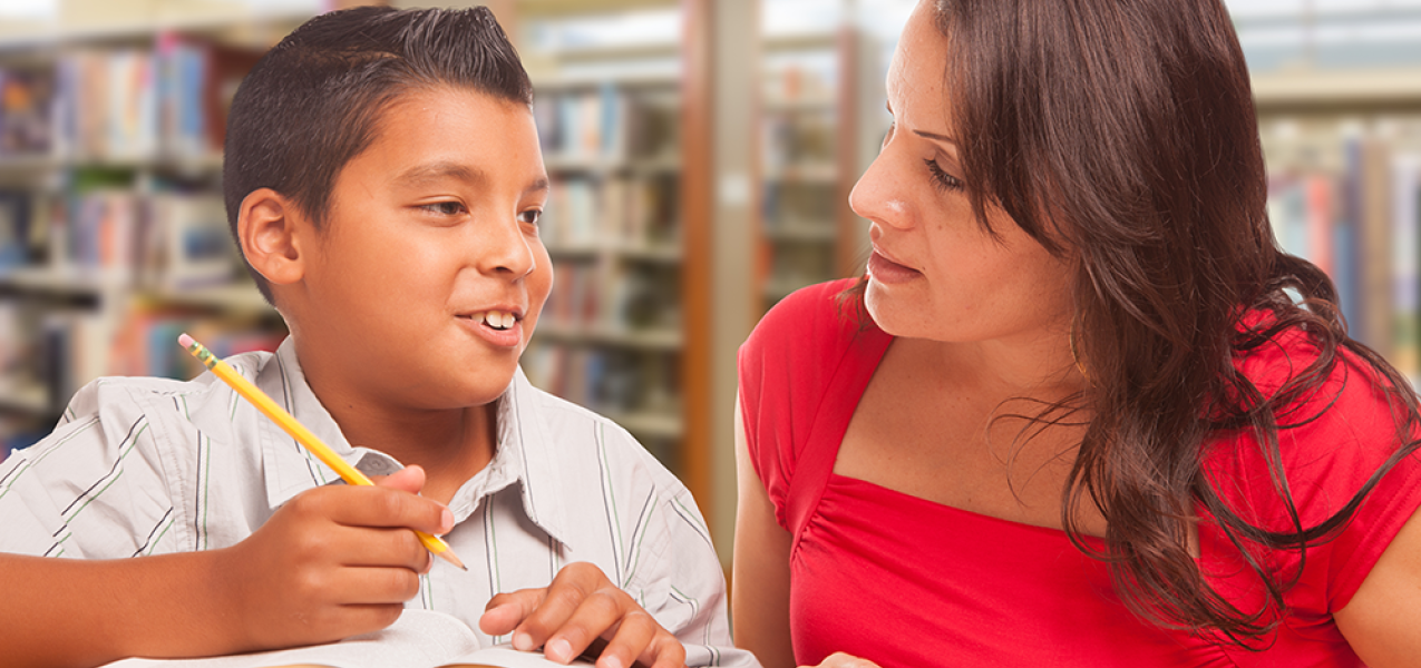 Young boy sits alongside tutor with open book between them