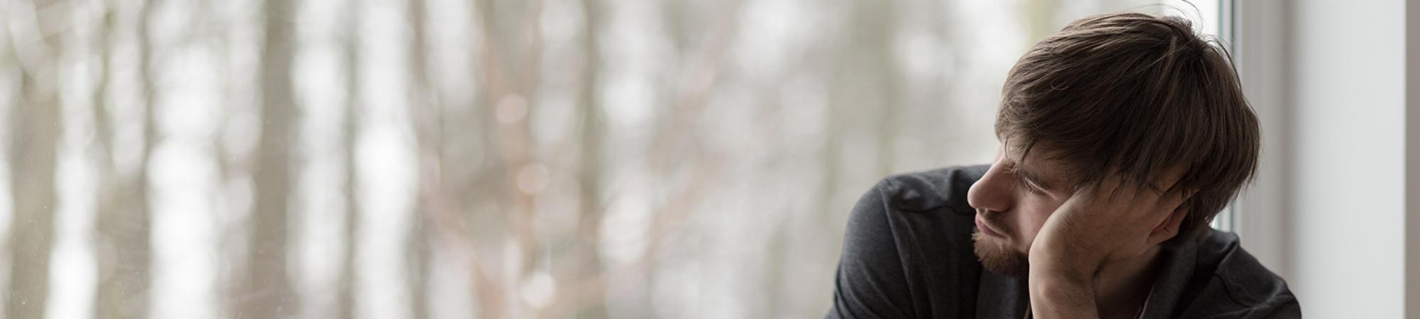 Man looking out window feeling overwhelmed