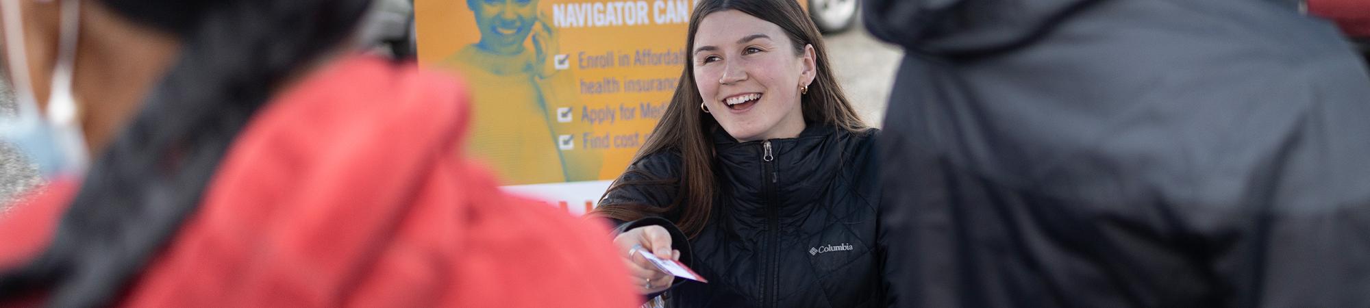 A person passing a card to two people at an event table.