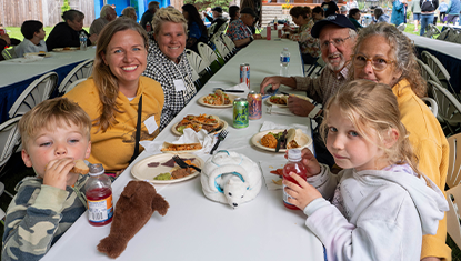 A family of six smiles at the camera under a tent at a picnic